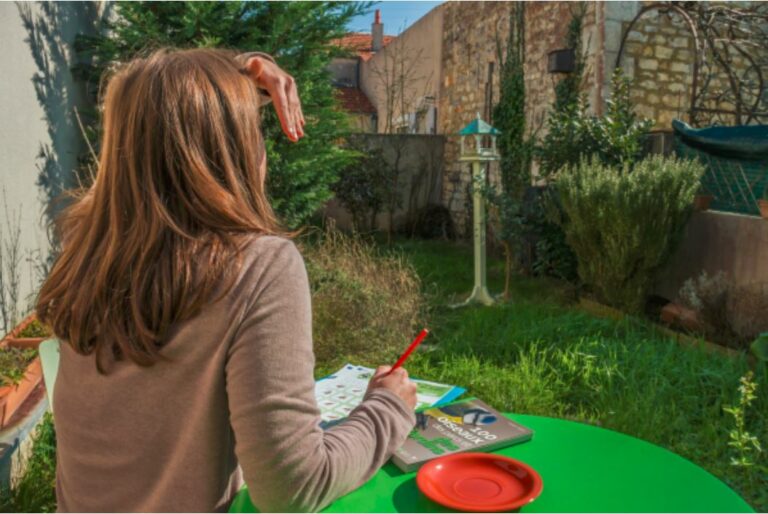 une femme observe et compte les oiseaux de son jardin assise à une table